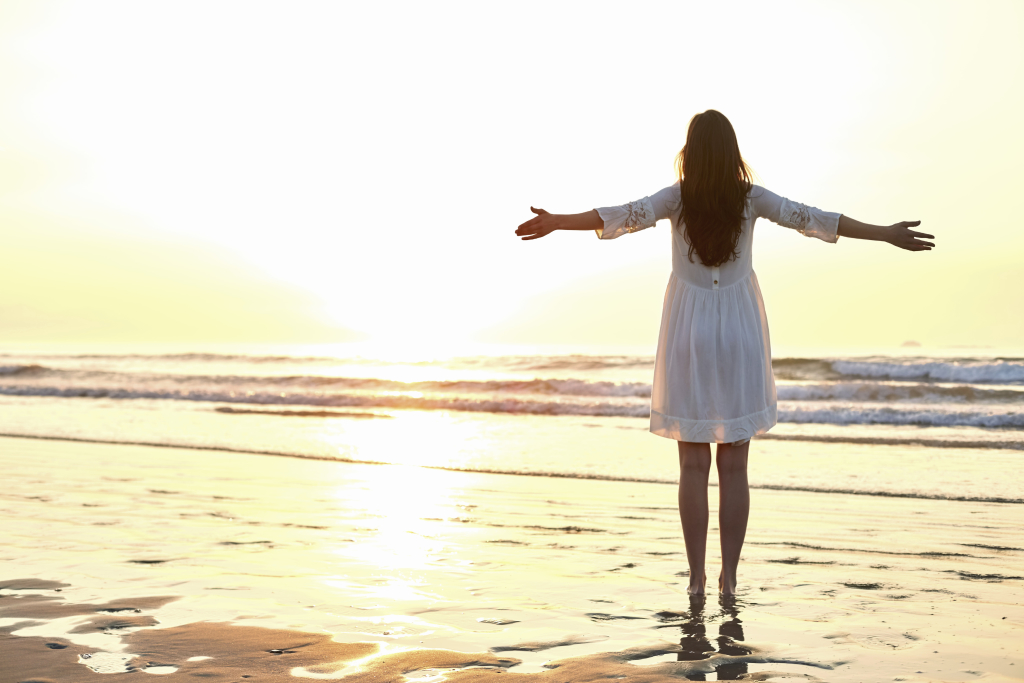 Woman standing arms outstretched on beach during sun